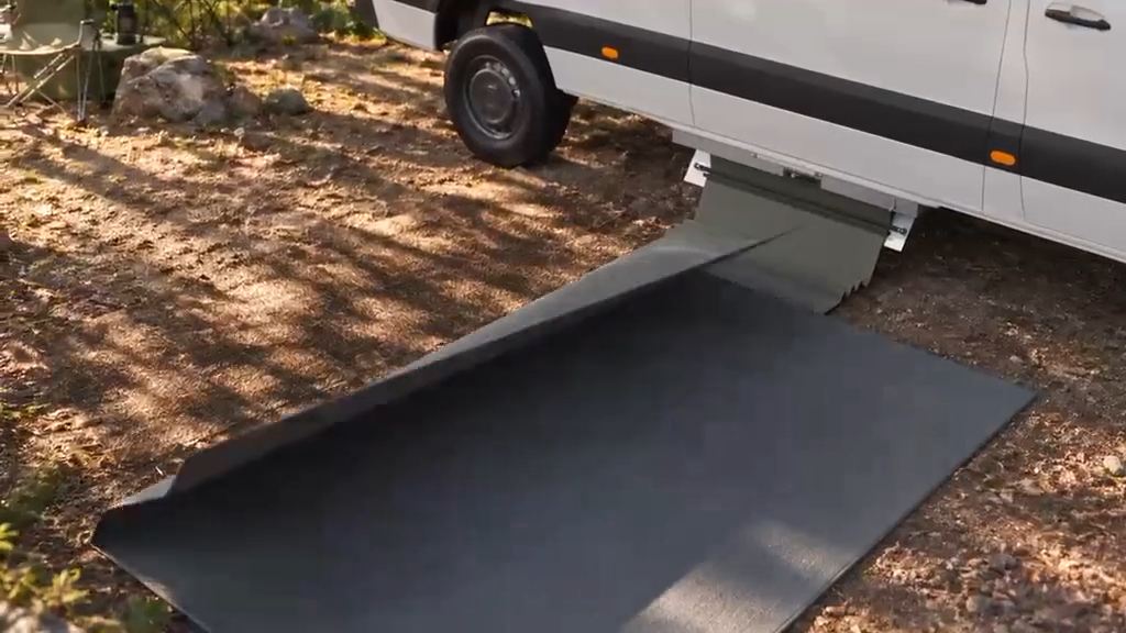 Concept render: a charcoal mat extended from under a camper van across a dirt campsite.